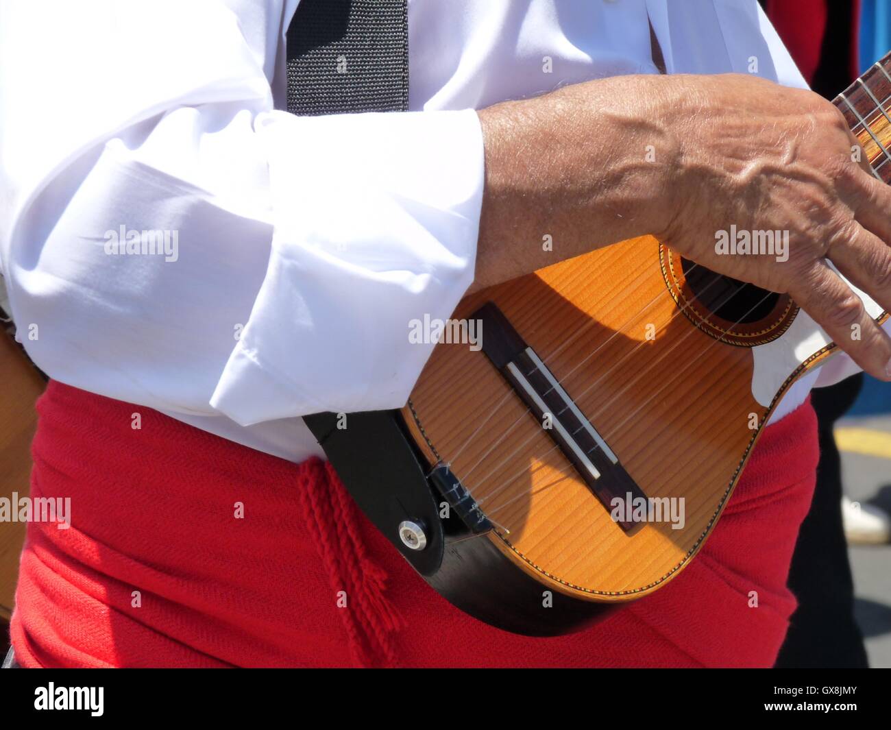 Close up di un canarino Islander indossando costumi regionali con colore rosso brillante anta, riproduzione di un 'timple', un tradizionale ukelele-come strumento Foto Stock