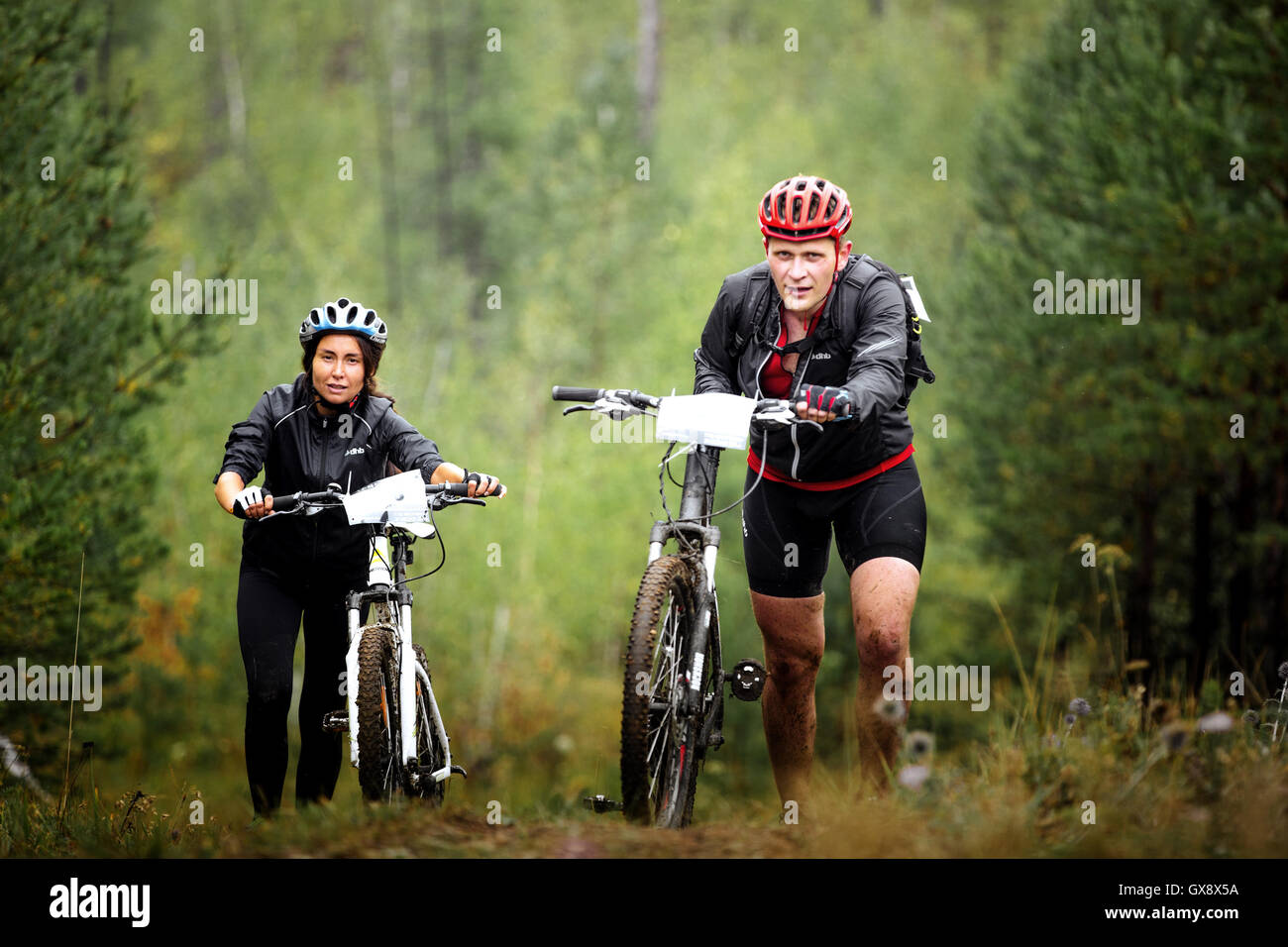 Coppia di maschio e femmina mountainbiker salire un passo in salita nel bosco durante gare regionali su cross-country bike Foto Stock