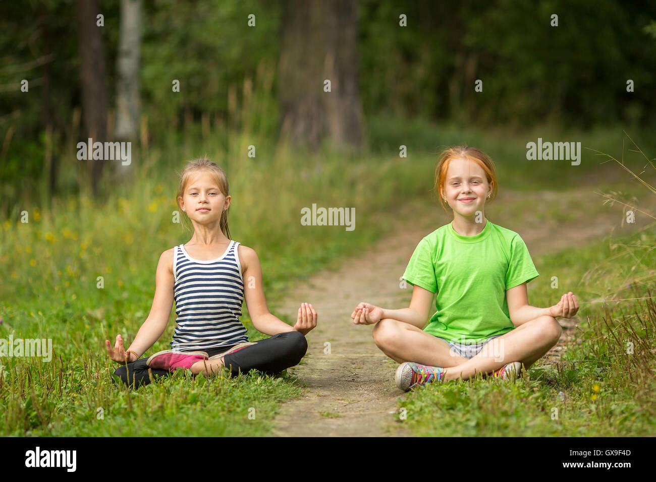 Due piccoli cute ragazze yoga seduti nella posizione del loto all'esterno. Foto Stock