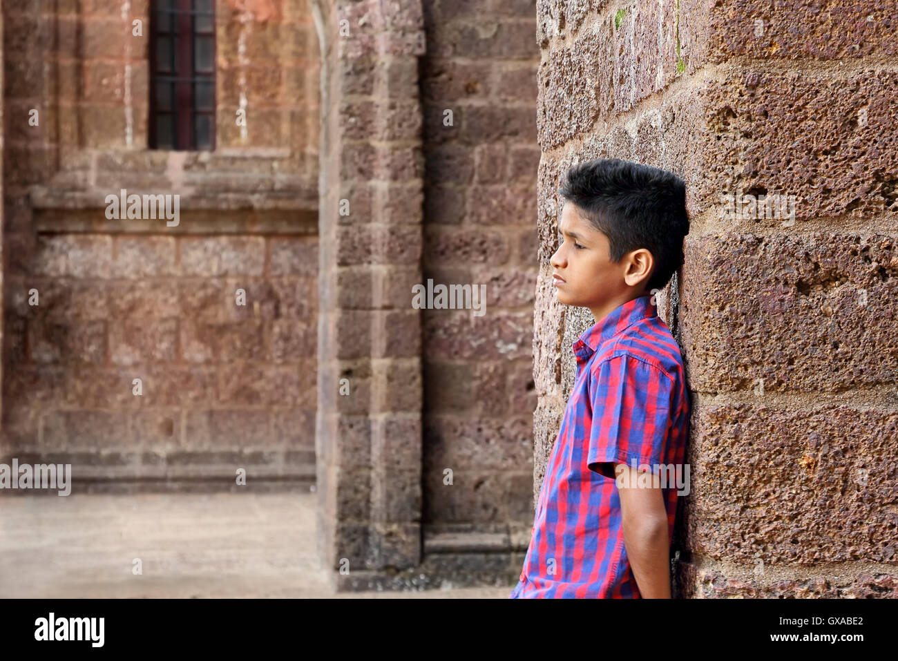 Teenage moody boy appoggiata contro il vecchio rosso muro di mattoni Foto Stock