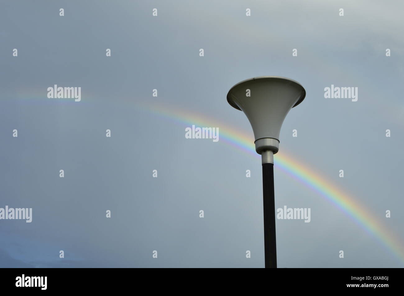 Illuminazione pubblica pole e Rainbow. Nuvole grigio sullo sfondo. Foto Stock