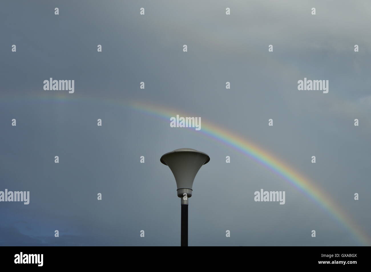 Illuminazione pubblica pole e Rainbow. Nuvole grigio sullo sfondo. Foto Stock