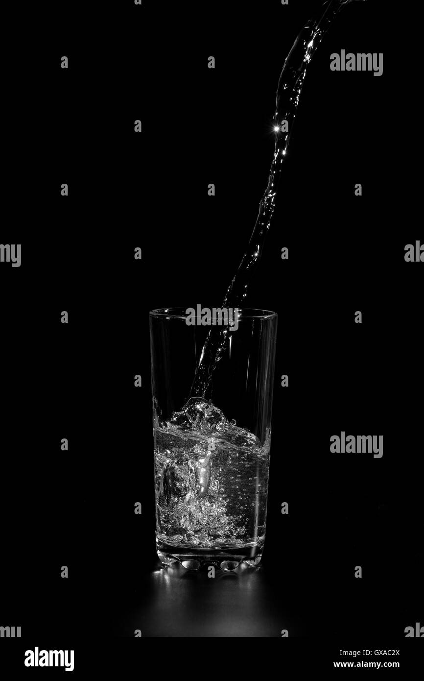 Flusso di acqua fresca versando in un bicchiere di vetro su uno sfondo scuro Foto Stock