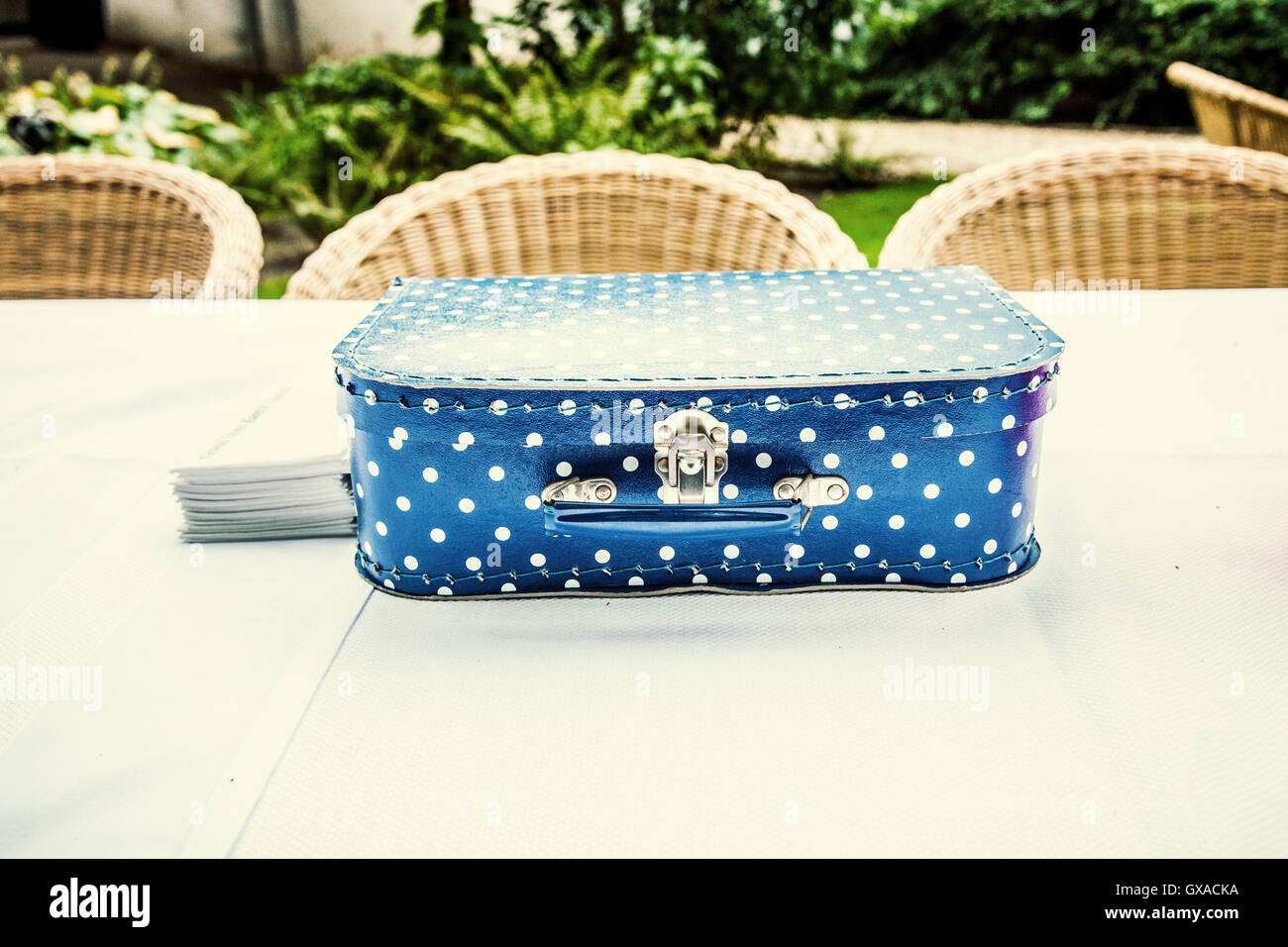 Bambino la valigia blu con puntini bianchi su un tavolo in un giardino sembra essere galleggiante sopra la tovaglia bianca. Foto Stock