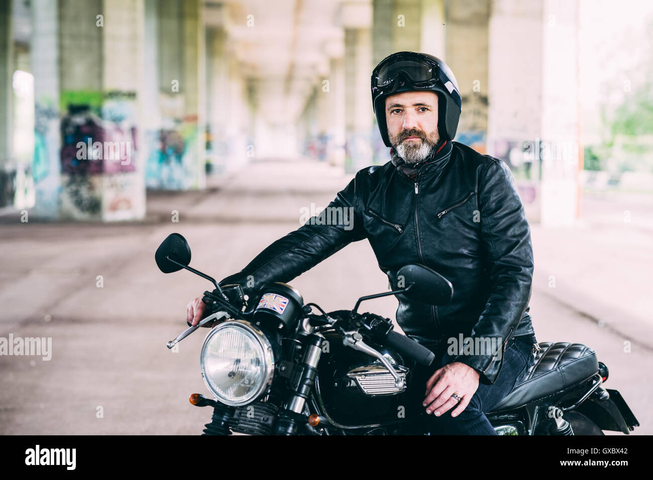 Maschio maturo motociclista seduto sul motociclo indossano casco sotto il cavalcavia Foto Stock