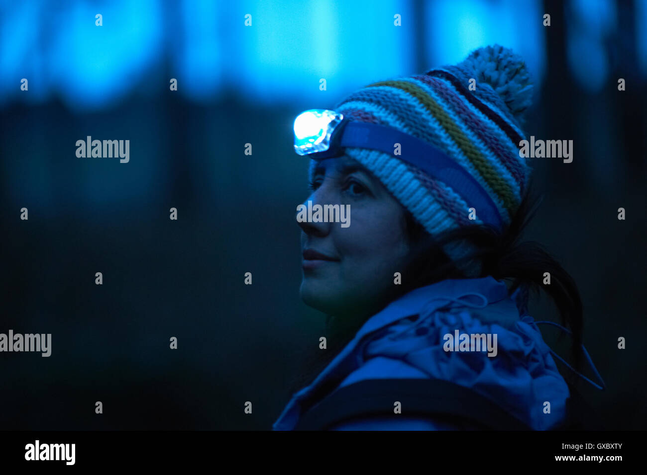 Escursionista femmina indossando la torcia da testa guardando sopra la sua spalla dalla foresta di notte Foto Stock