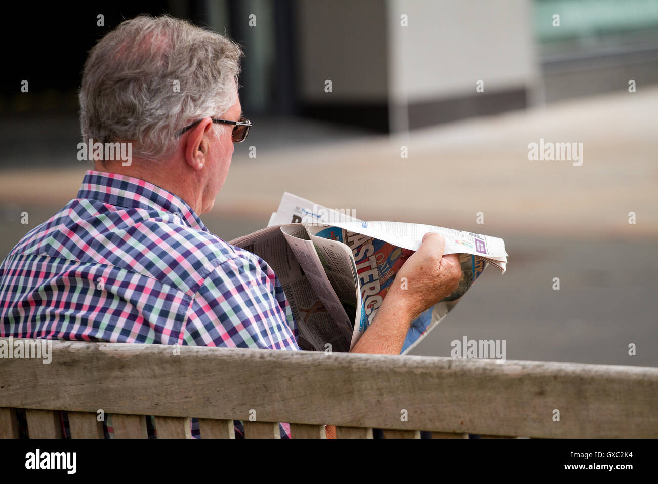 Un anziano uomo seduto su un sedile di estate la lettura del lunedì il Giornale di posta nel centro di Dundee, Regno Unito Foto Stock