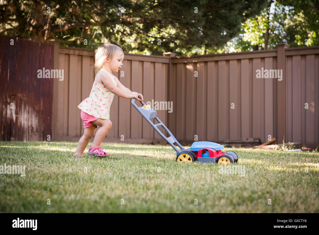 Giovane ragazza in giardino, spingendo toy tosaerba Foto Stock
