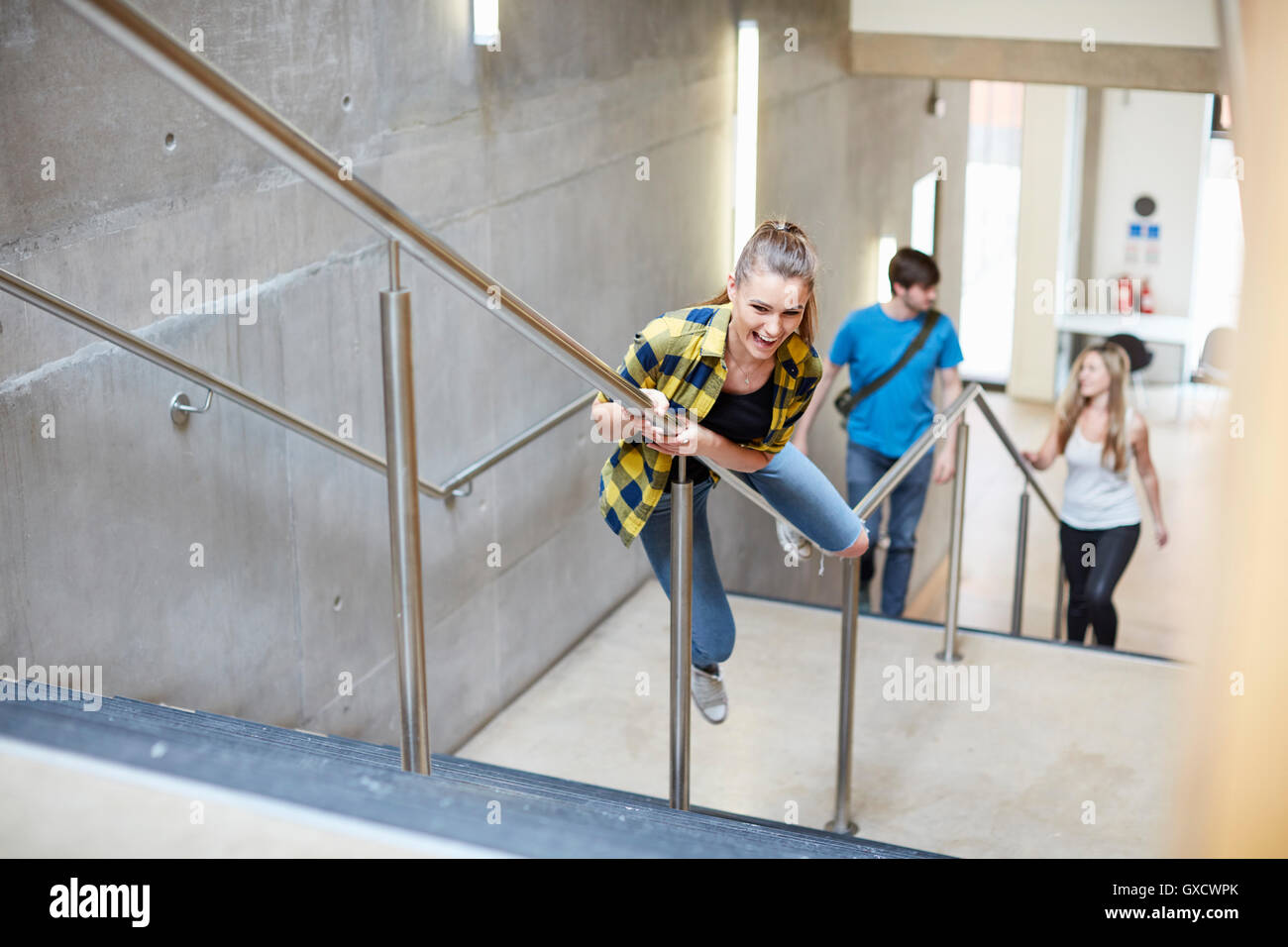 Giovane studentessa lo scorrimento verso il basso del corrimano scalinata a istituti di istruzione superiore college Foto Stock