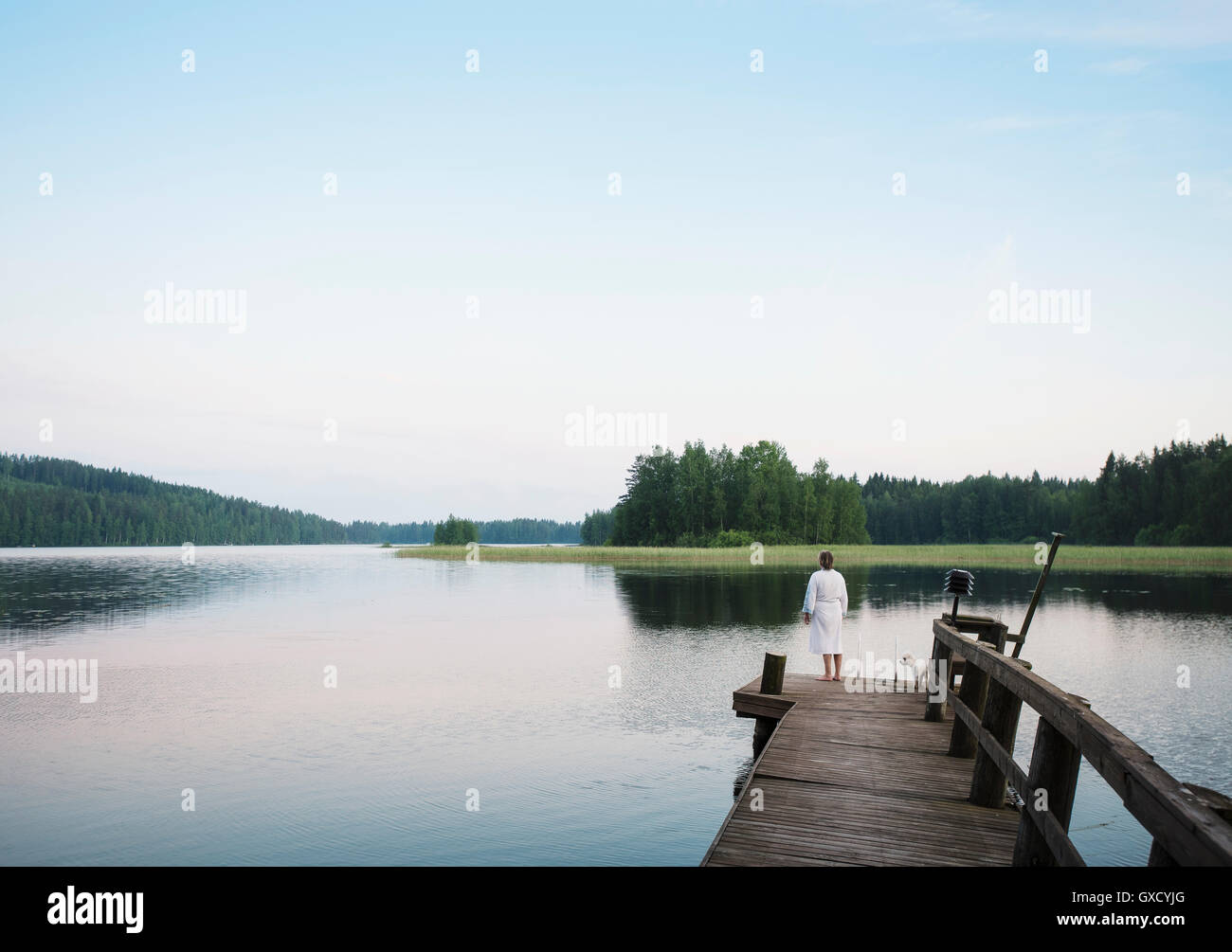 Donna che indossa accappatoio con coton de tulear cane guardando fuori dal lago di pier, Orivesi, Finlandia Foto Stock