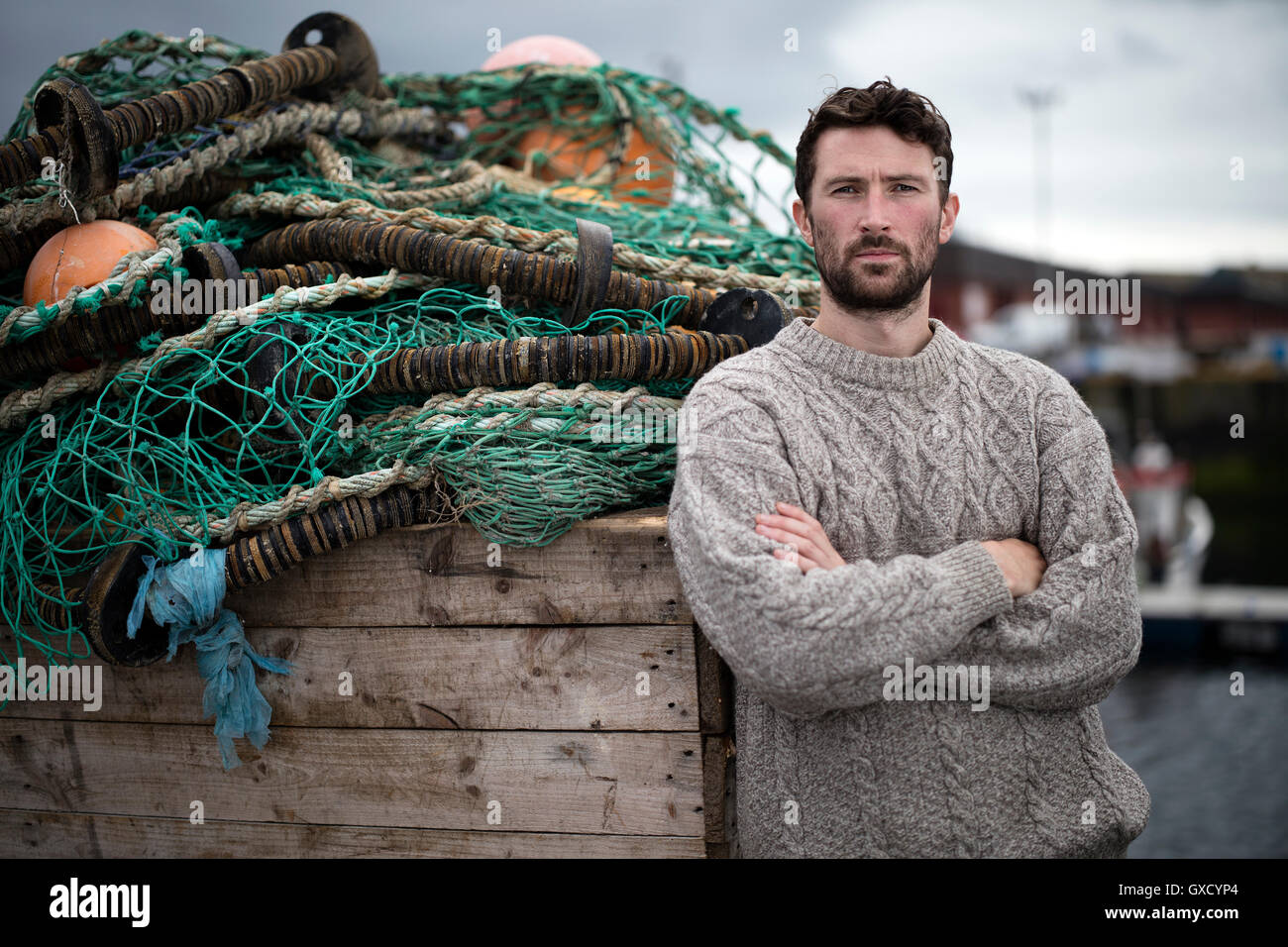 Ritratto di giovane pescatore appoggiata contro la cassa di reti da pesca in porto, Fraserburgh, Scozia Foto Stock