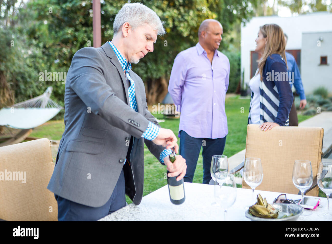 Uomo maturo stappo bottiglia di vino al party in giardino tavolo Foto Stock