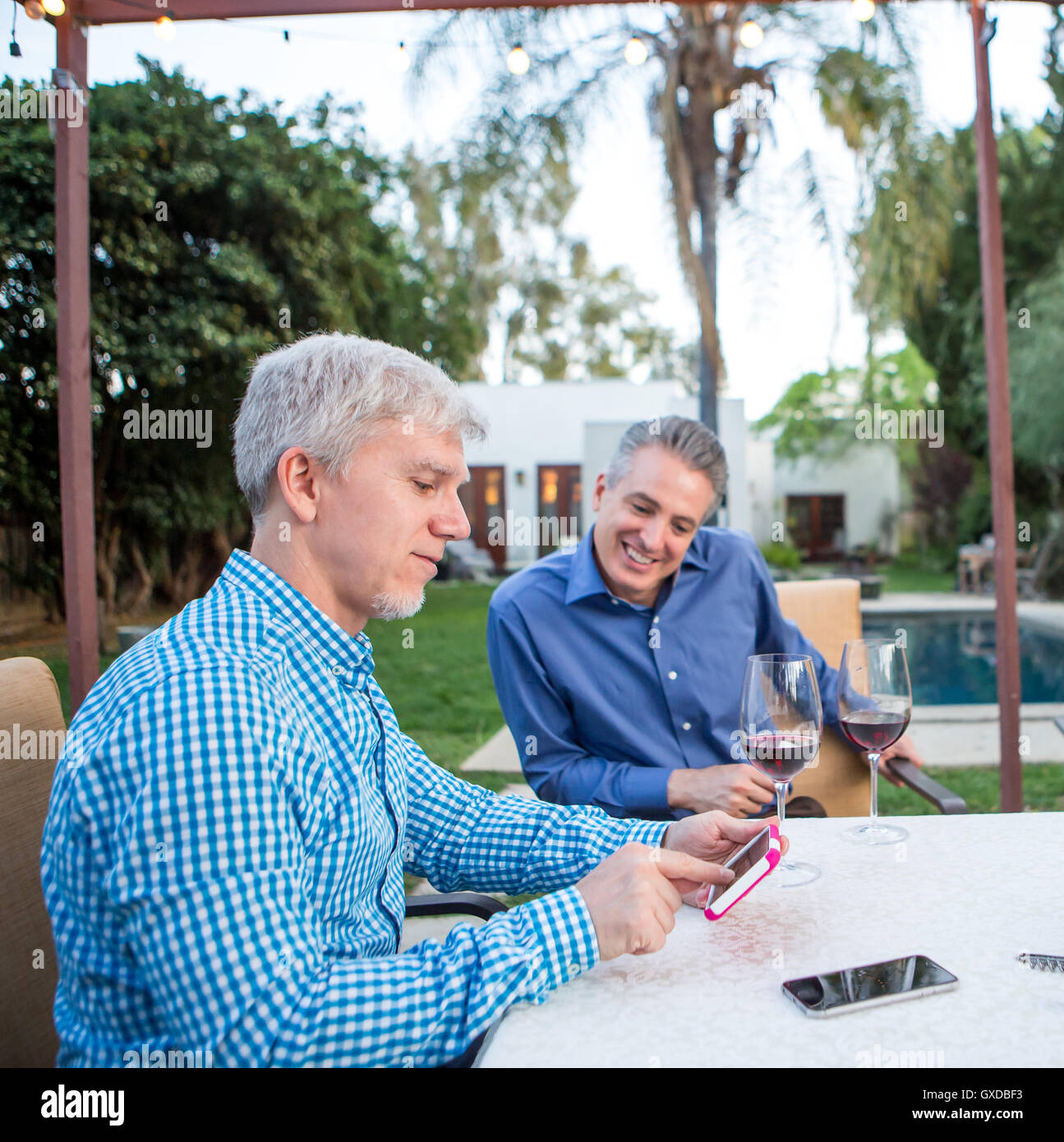 Due uomini maturi guardando il touchscreen dello smartphone al party in giardino tavolo Foto Stock