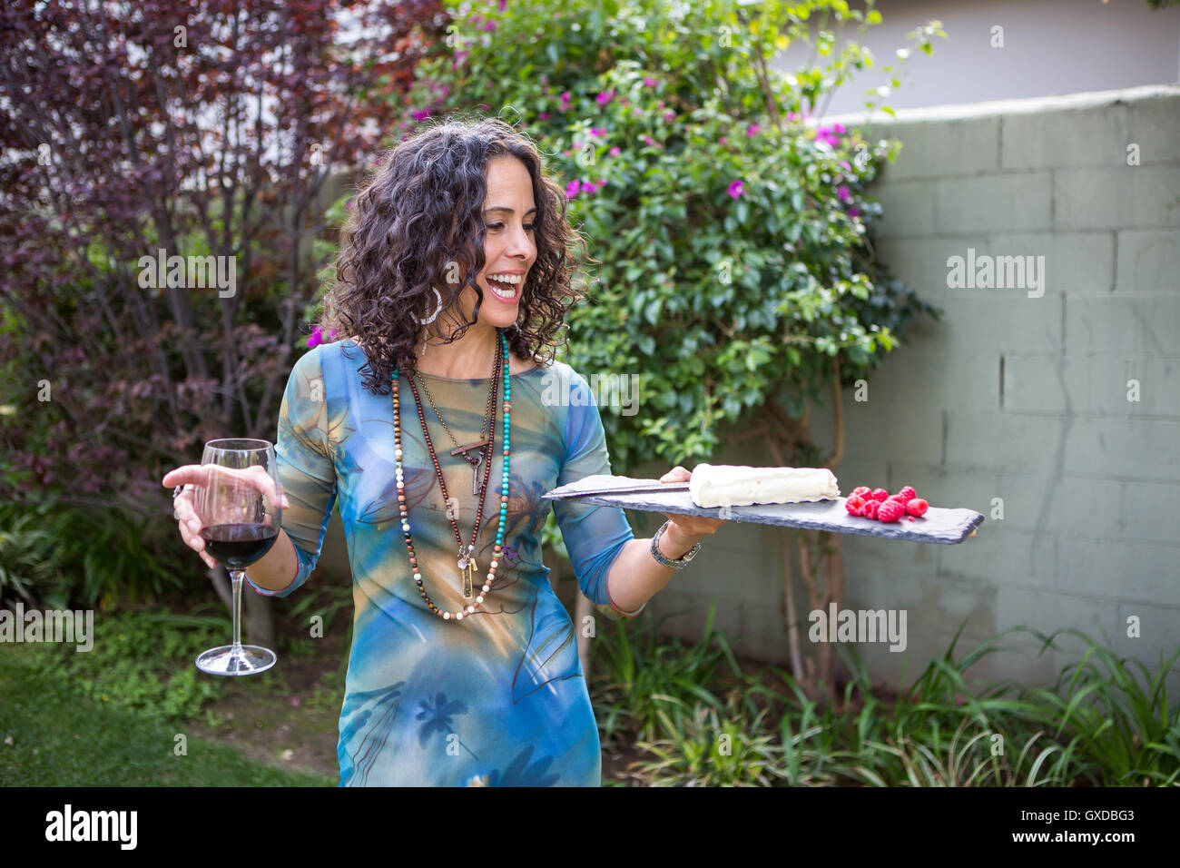 Donna matura azienda tagliere e vino rosso al party in giardino Foto Stock