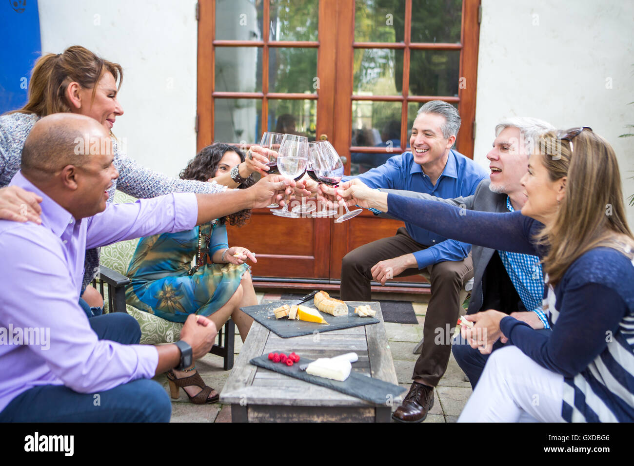 Sei adulti maturi amici vinificazione toast al garden party sul patio Foto Stock