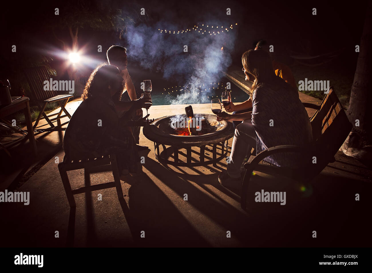 Quattro adulti maturi sedersi insieme attorno ad un patio fuoco di notte Foto Stock