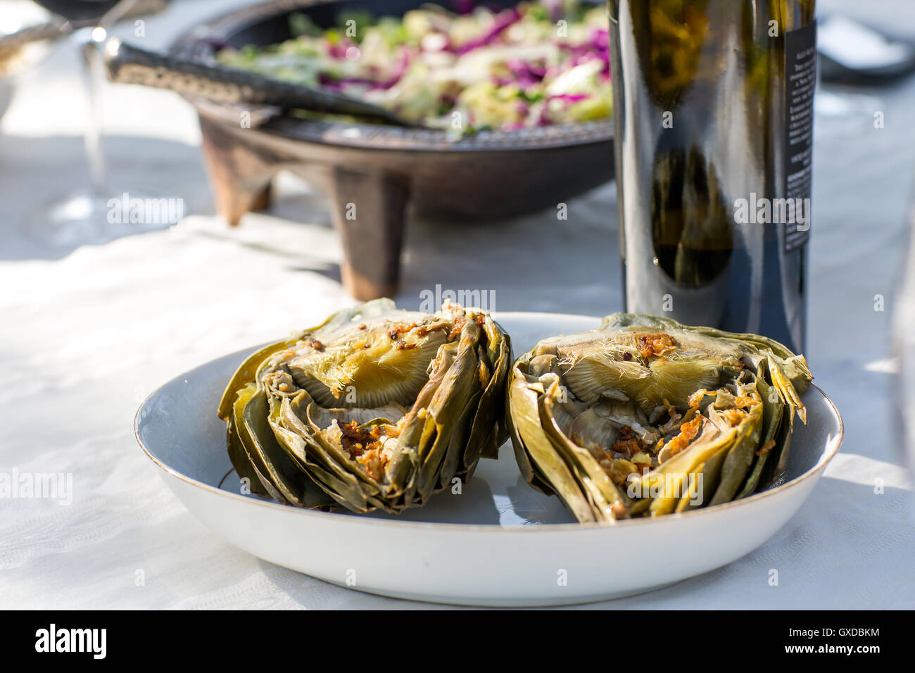 Parte Tavolo da giardino con bottiglia di vino e carciofi cotti al forno Foto Stock