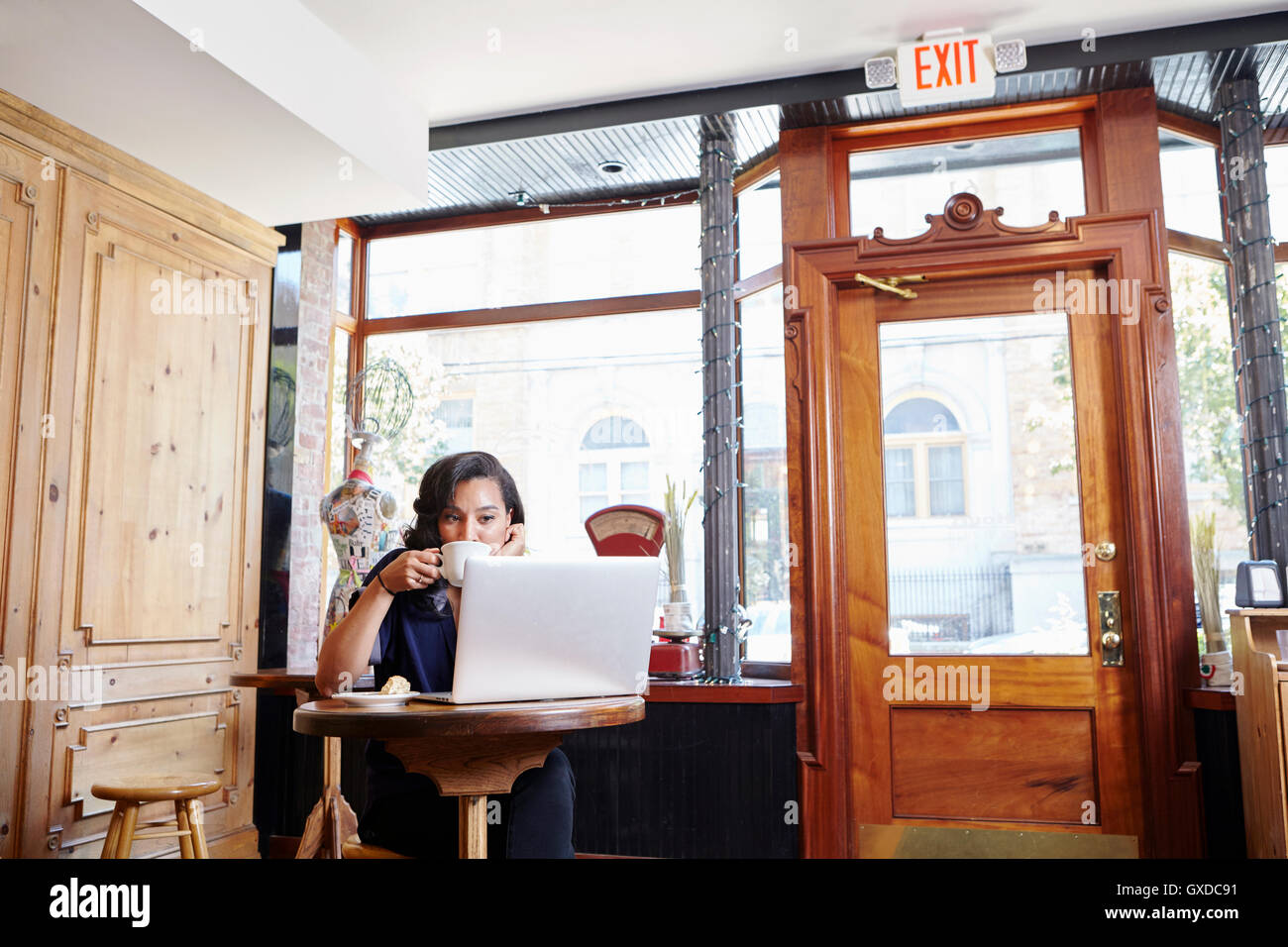 Giovane donna seduta al cafe, bere caffè, utilizzando laptop Foto Stock