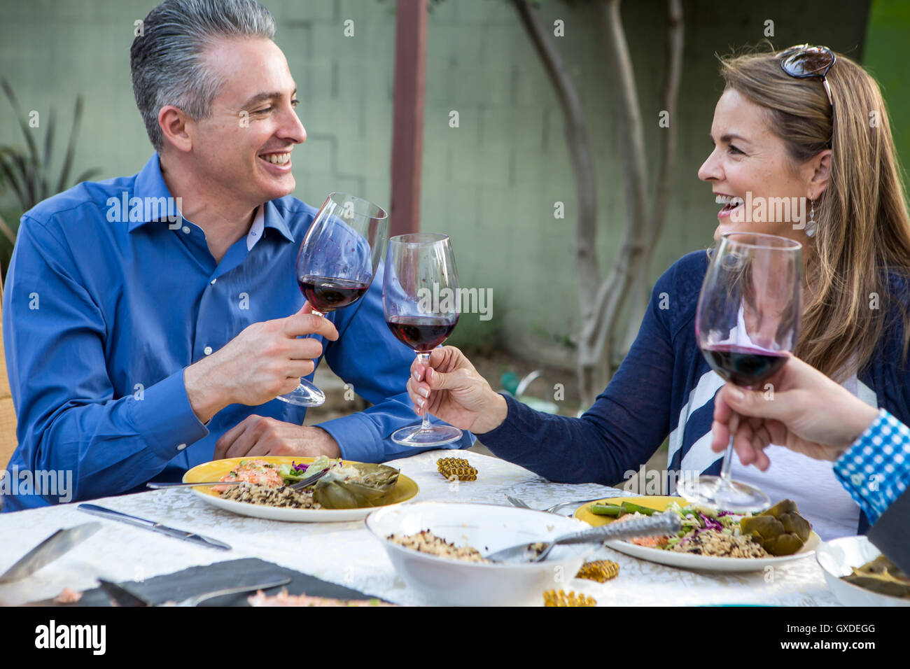 Coppia di amici facendo un vino rosso toast al party in giardino tavolo Foto Stock