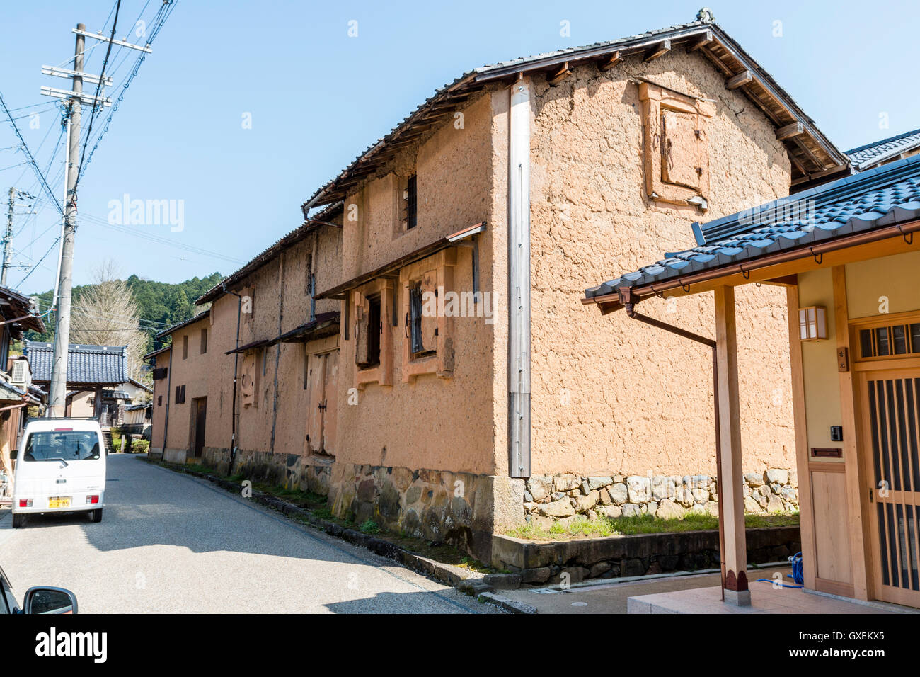 Giappone, Izushi. Street con il rosso fango parete spiovente edificio, a saka birreria a partire dal periodo Meiji, manfacturing 'Sasazru' saki locale. Cielo blu chiaro. Foto Stock