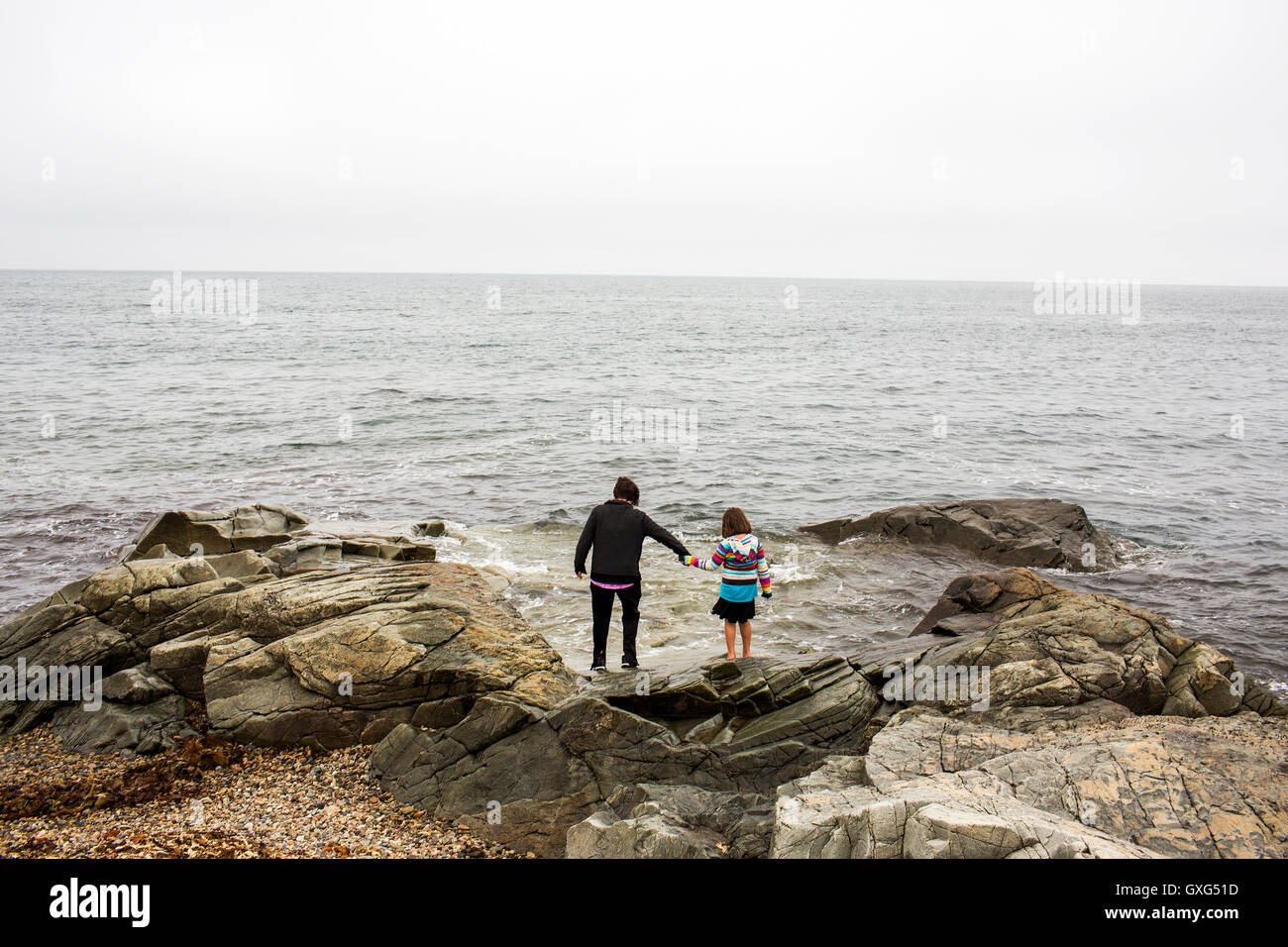 Caucasian madre e figlia tenendo le mani sulle rocce a ocean Foto Stock