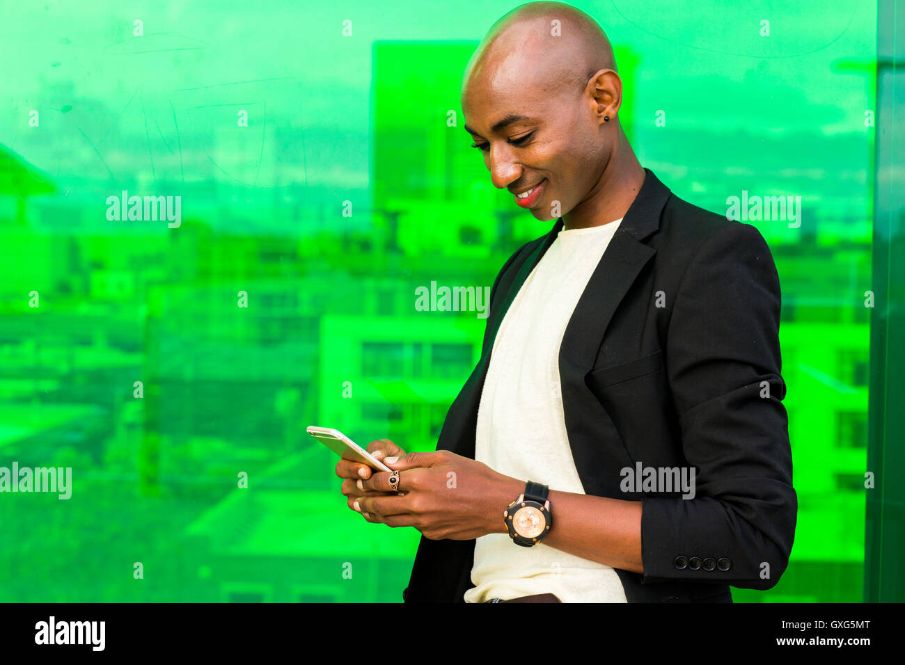 Sorridente gay uomo nero texting vicino a finestra verde Foto Stock