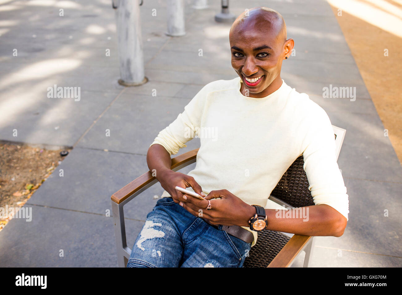 Sorridente gay uomo nero texting in cattedra all'aperto Foto Stock