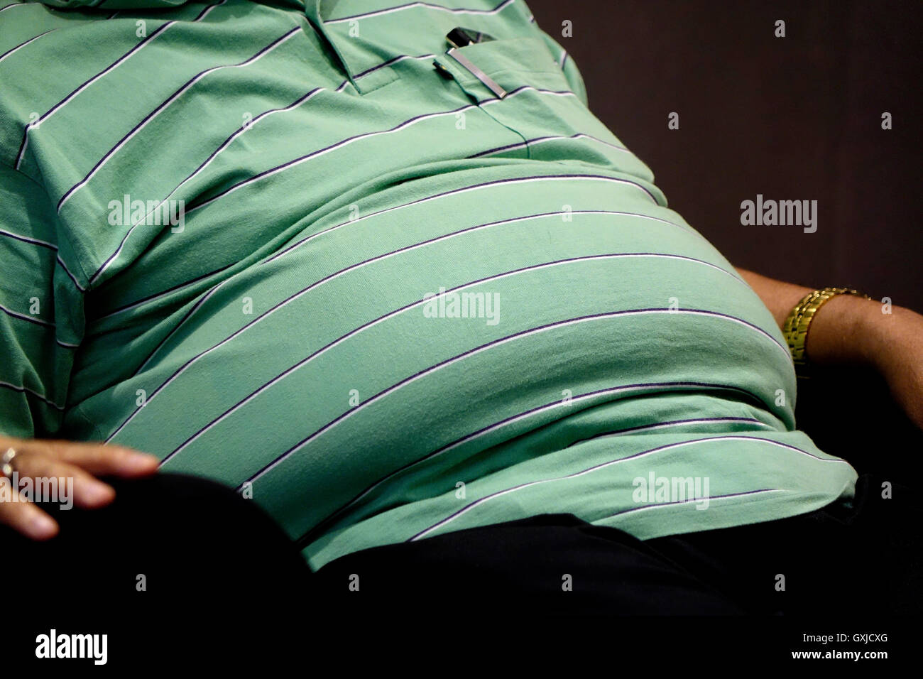 Pancia,l'obesità,flab,sovrappeso,l'uomo,indiana, striped shirt,seduta,slump,Panza,fat,,T-shirt.tee shirt Foto Stock