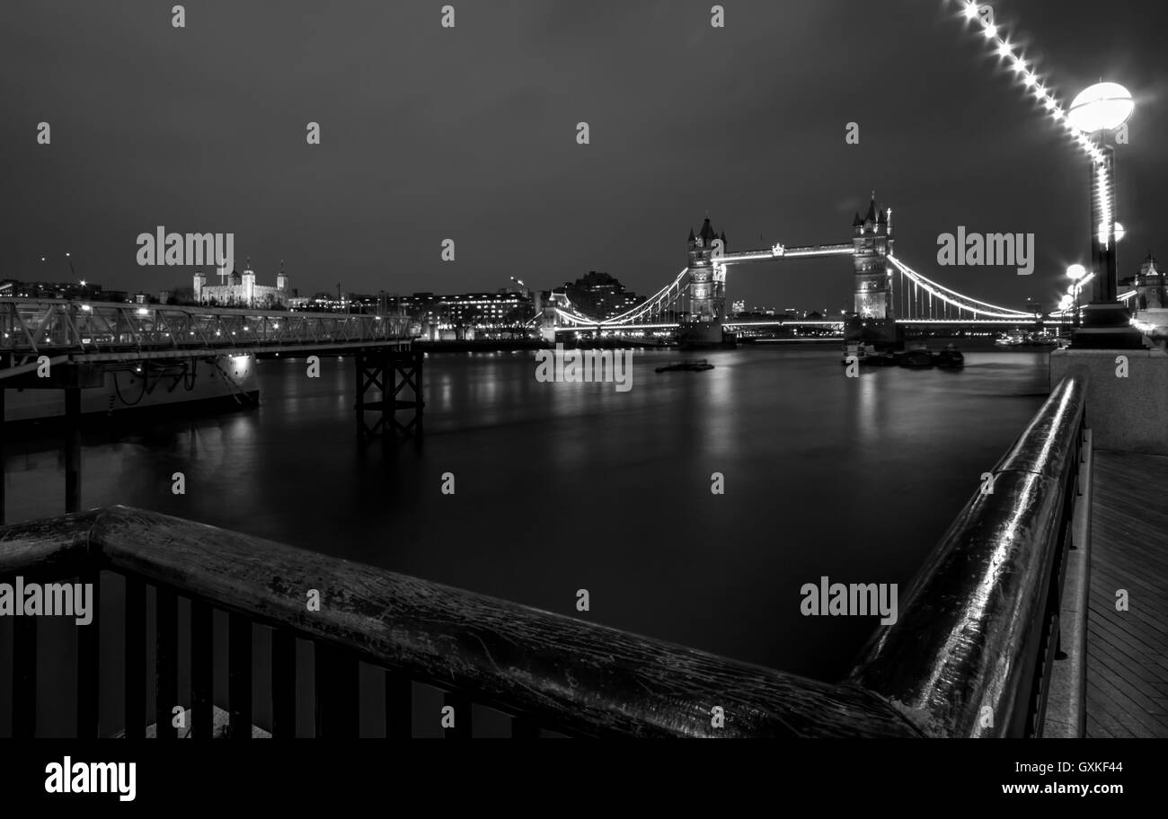 Il Tower Bridge è illuminato di notte. Utilizzando una lunga esposizione per regolare le acque del fiume Tamigi, Marzo. Convertito in bianco e nero Foto Stock