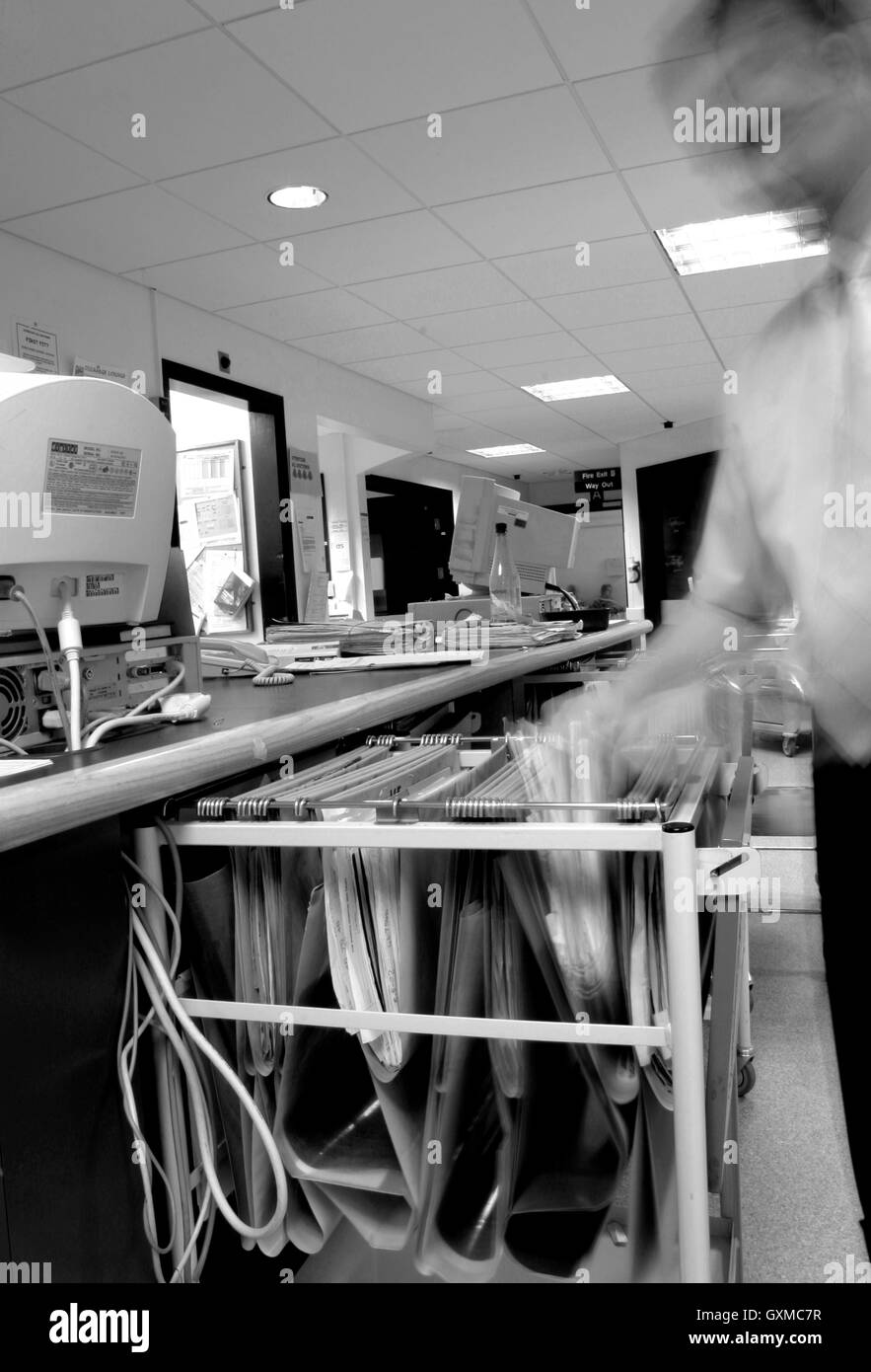 Un giovane NHS medico o infermiere apre il paziente medical records disegnare in ward la ricezione di un segnale di occupato locale ospedale NHS Foto Stock