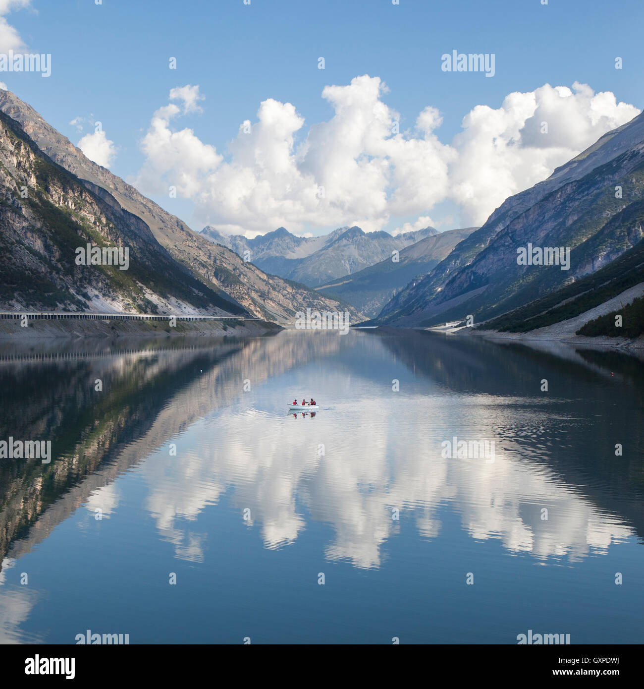 Lago di alta montagna con barca, acqua fredda e i riflessi di un cielo blu e nuvole. Foto Stock