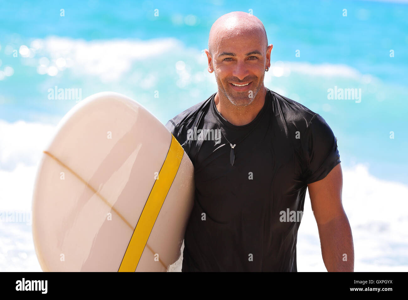 Ritratto di un uomo bello con tavola da surf in mano, bei surf trainer sulla spiaggia, godendo di sport d'acqua, attivi in estate Foto Stock