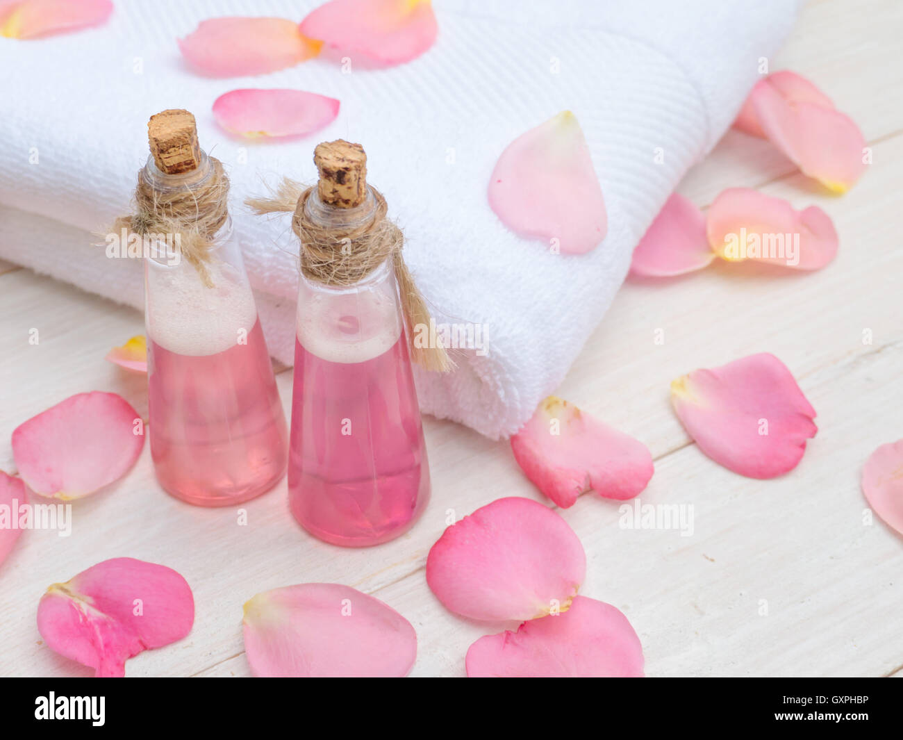 Shampoo rosa in piccoli flaconi, asciugamano bianco e rosa petali di rosa Foto Stock