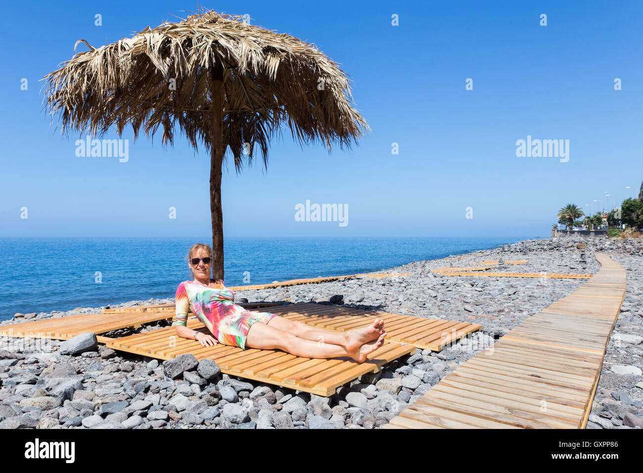 Caucasian donna di mezza età a prendere il sole come turista sulla spiaggia sassosa in Madeira Foto Stock