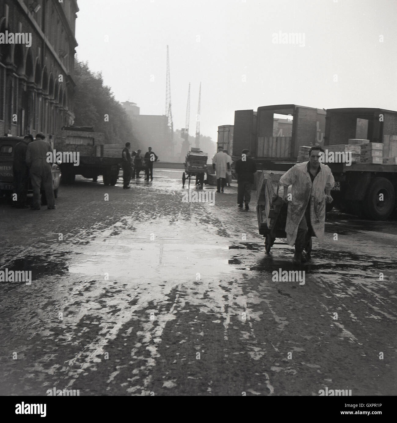 Degli anni Cinquanta, storico mercato tira porter carrello caricato con piatti di pesce fresco al di fuori del mercato del Pesce di Billingsgate, Londra. Foto Stock