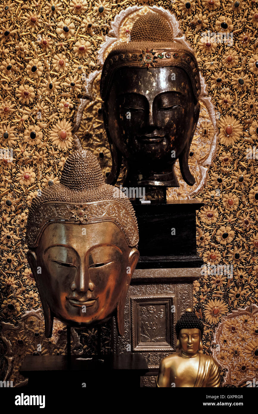 Diverse statue di Buddha con uno sfondo decorativo e ornato in vendita in un negozio di souvenir a Bangkok in Thailandia. Le caratteristiche distintive delle teste di Buddha, come i capelli corti e ricci, simboleggiano la rinuncia del Buddha al suo passato privilegiato. Foto Stock
