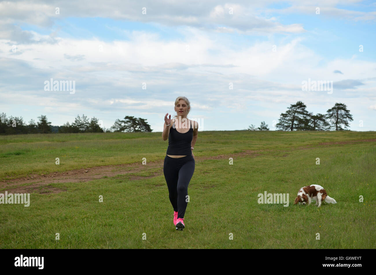 Donna jogging nella natura nel pomeriggio mentre il suo cane è in esecuzione accanto a lei Foto Stock