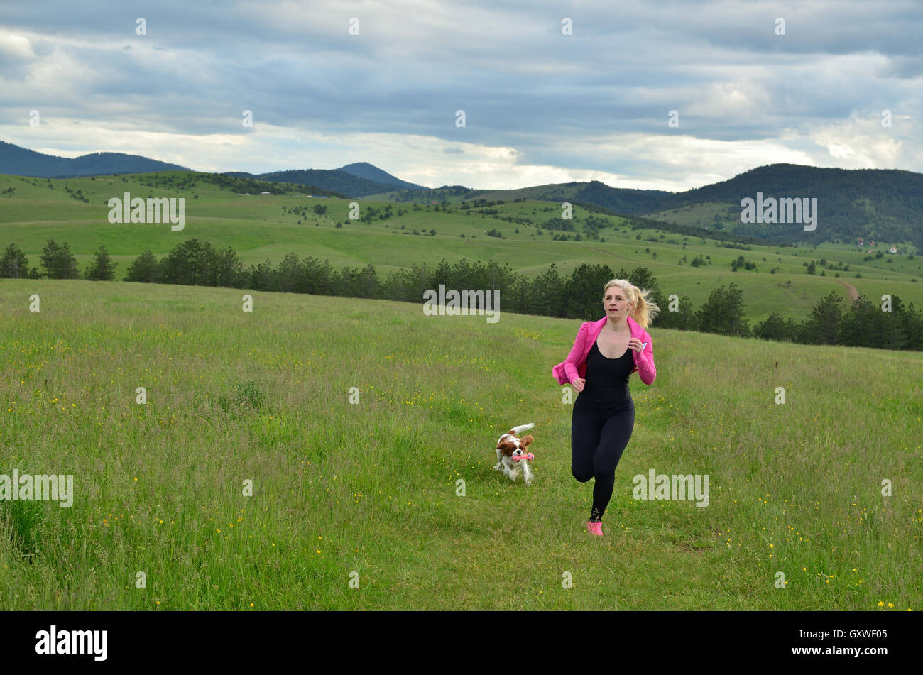 Signora in rosa e nero sportswear jogging con il suo cane in orizzontale in un giorno nuvoloso Foto Stock