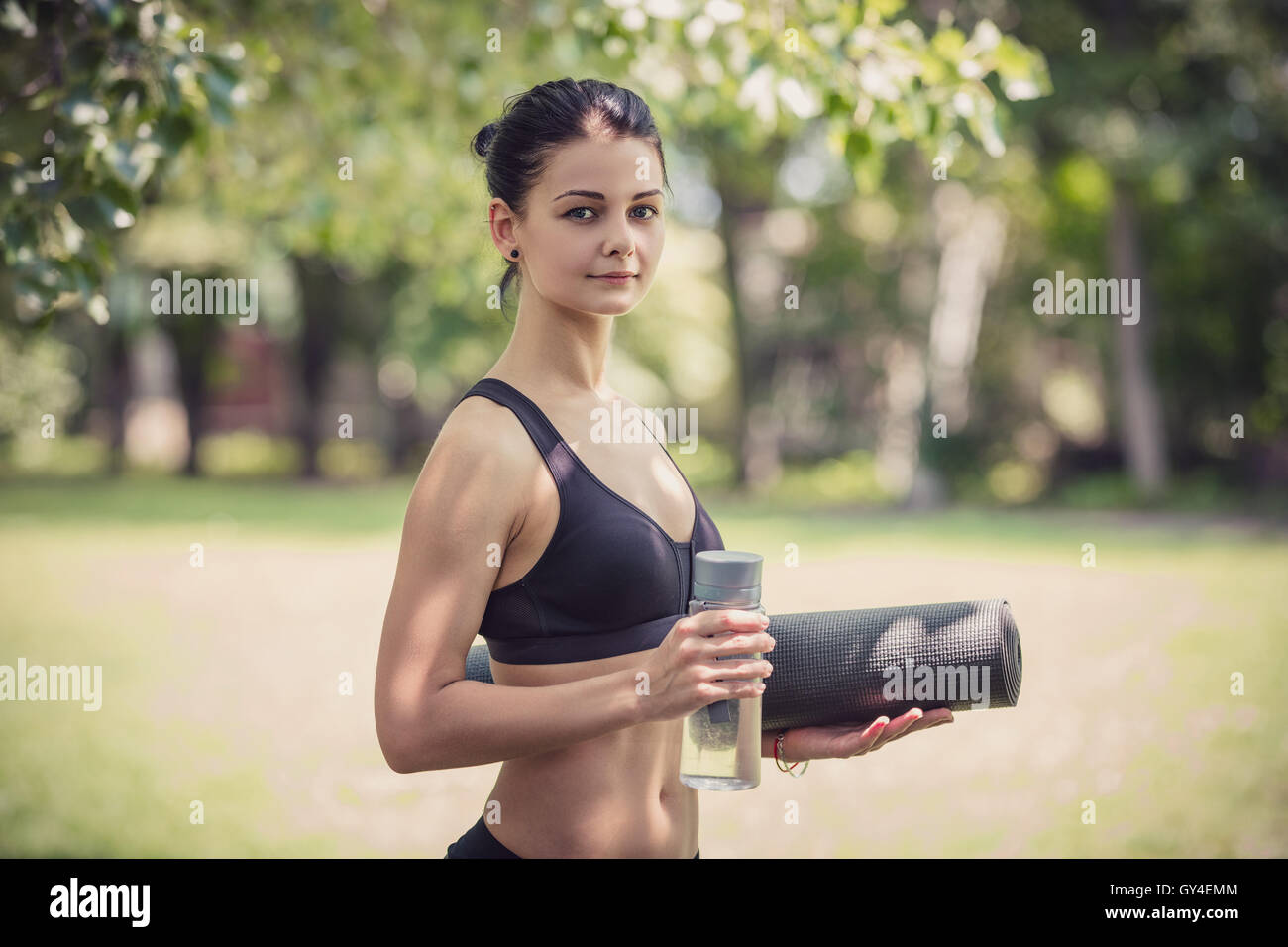 Giovane donna in abbigliamento sportivo tenendo una bottiglia di acqua minerale e materassino yoga Foto Stock
