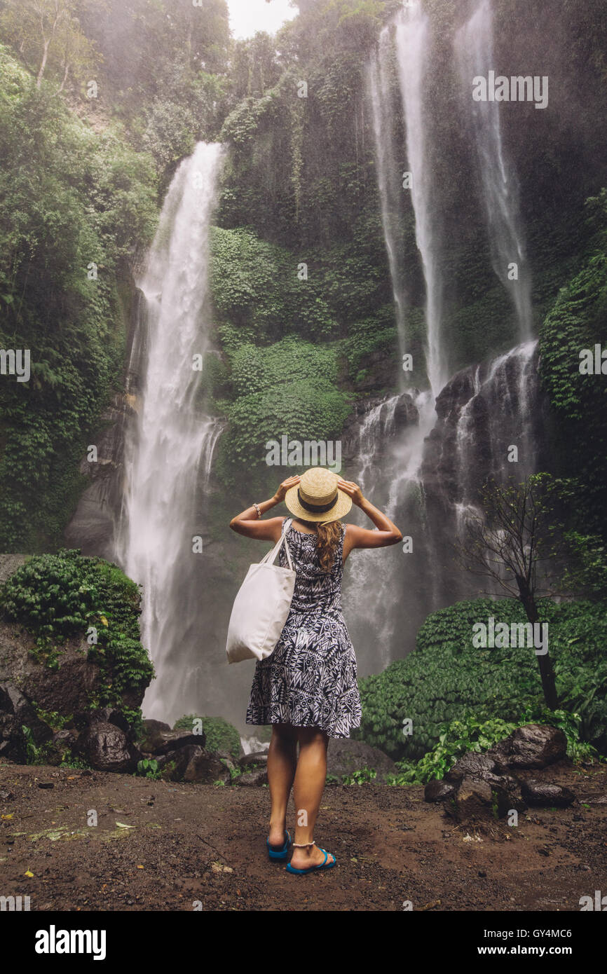 Vista posteriore del colpo di turista femminile ammirando bella cascata nella foresta pluviale tropicale. Giovane donna che guarda la cascata. Foto Stock