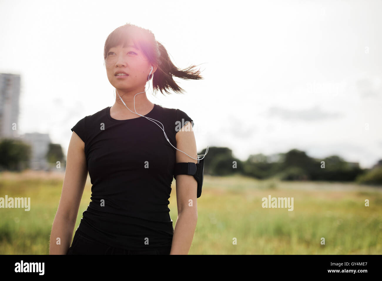 Colpo di giovane donna in abbigliamento sportivo in piedi all'aperto nel parco della città sulla giornata di sole e guardando lontano. Femmina cinese runner pronti per Foto Stock