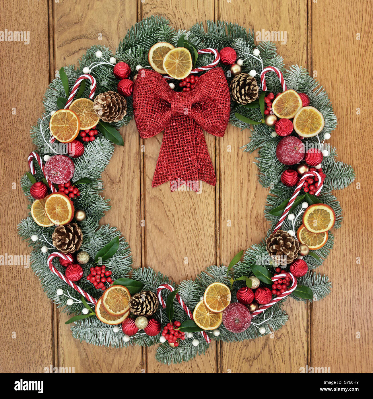 Ghirlanda di Natale con fiocco rosso decorazione, frutta secca, candy  canes, baubles, agrifoglio, vischio, pigne e coperta di neve fir Foto stock  - Alamy