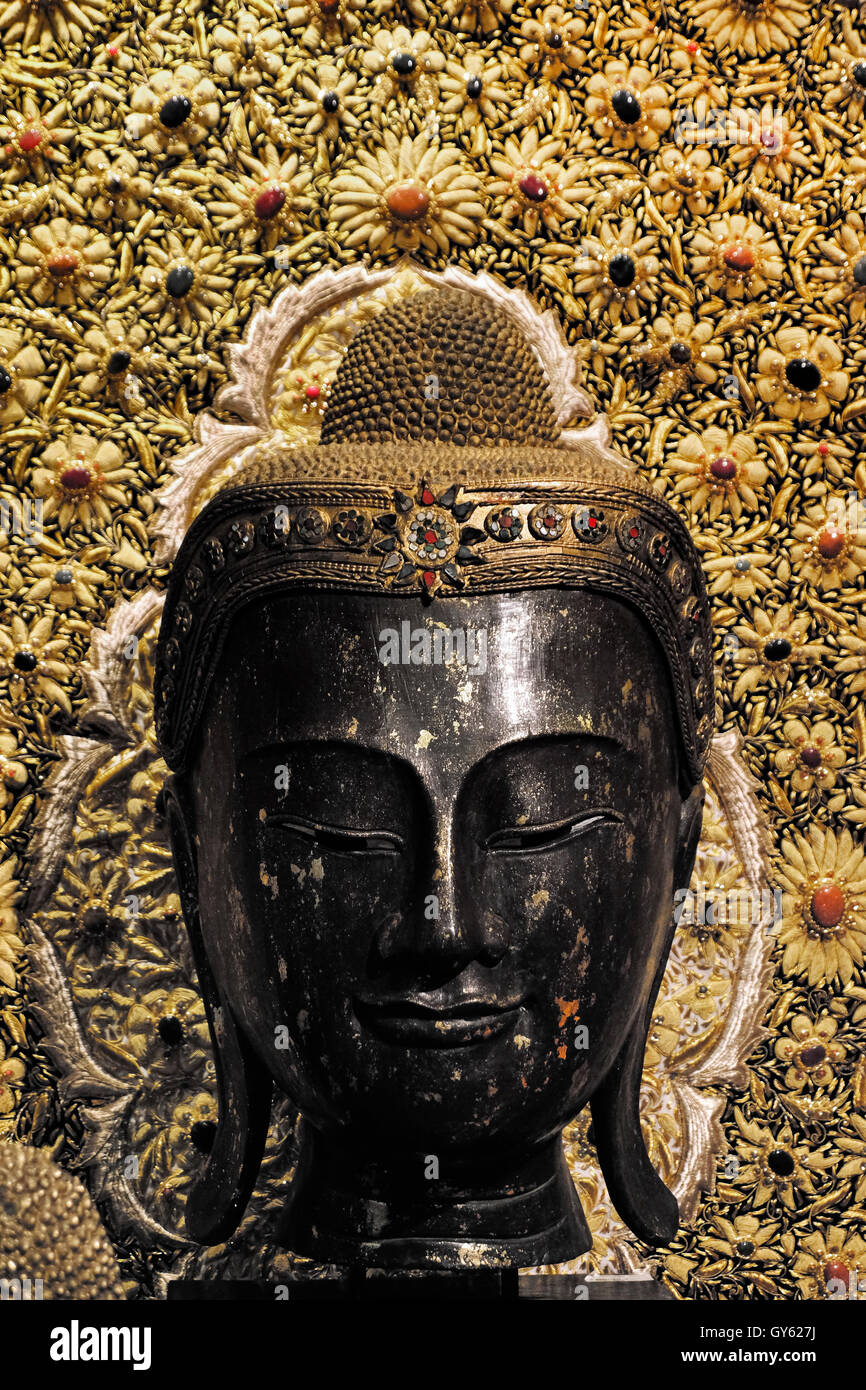 Statua del Buddha con sfondo decorativo e ornato in vendita in un negozio di souvenir a Bangkok in Thailandia. Le caratteristiche distintive delle teste di Buddha, come i capelli corti e ricci, simboleggiano la rinuncia del Buddha al suo passato privilegiato. Foto Stock