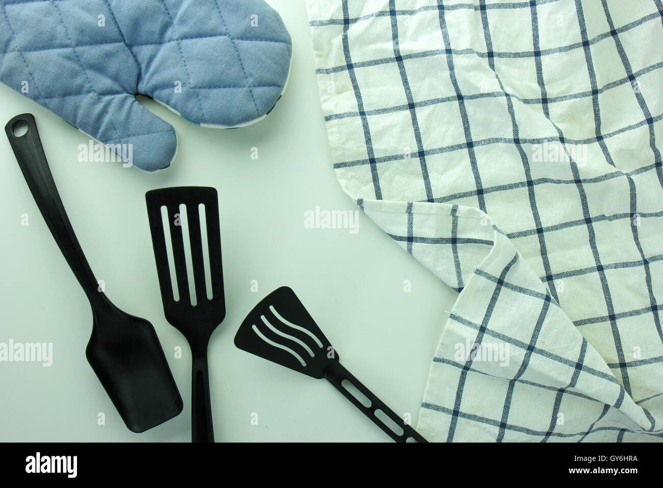 Siviera nero, guanto da forno e spade di padella sul tavolo bianco Foto Stock