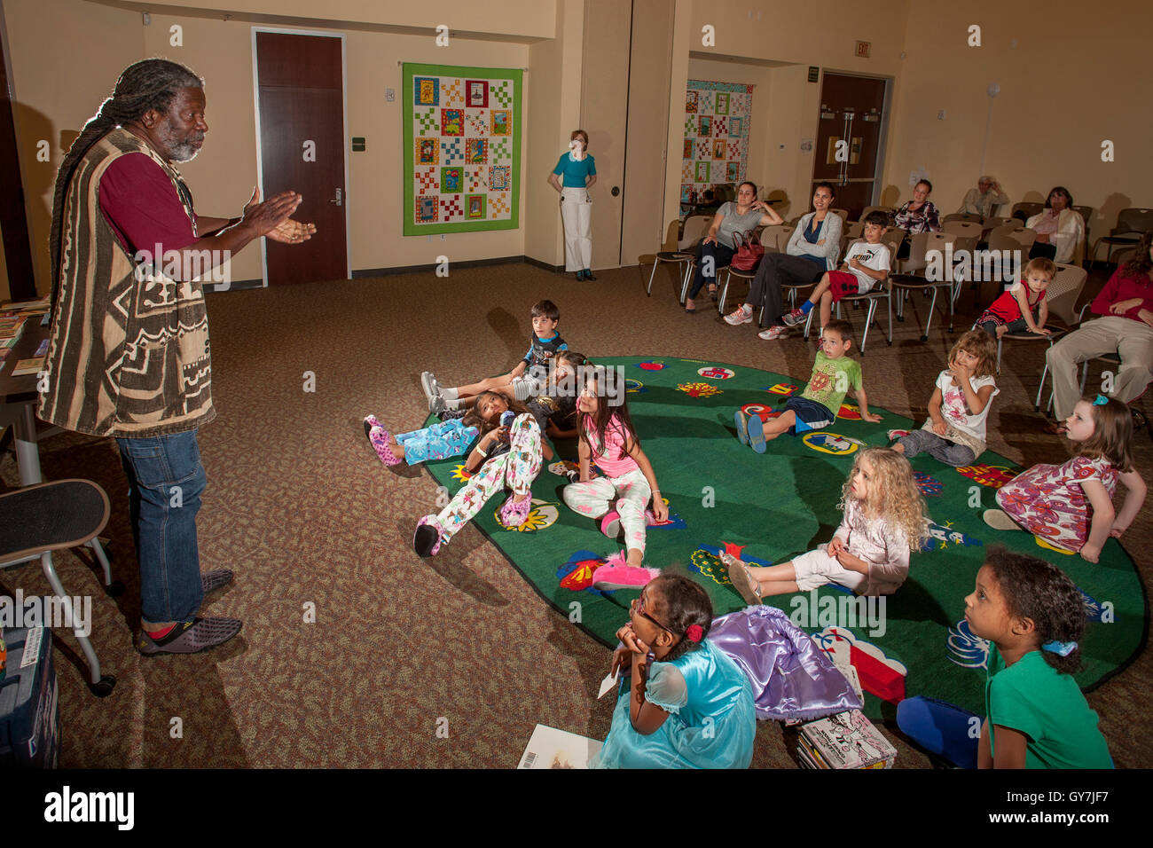 I bambini ascoltare un narratore professionali relative racconti africani come i loro genitori puoi ascoltare la musica in una biblioteca pubblica sala polivalente in Laguna Niguel, CA. Nota camicia colorati. Foto Stock