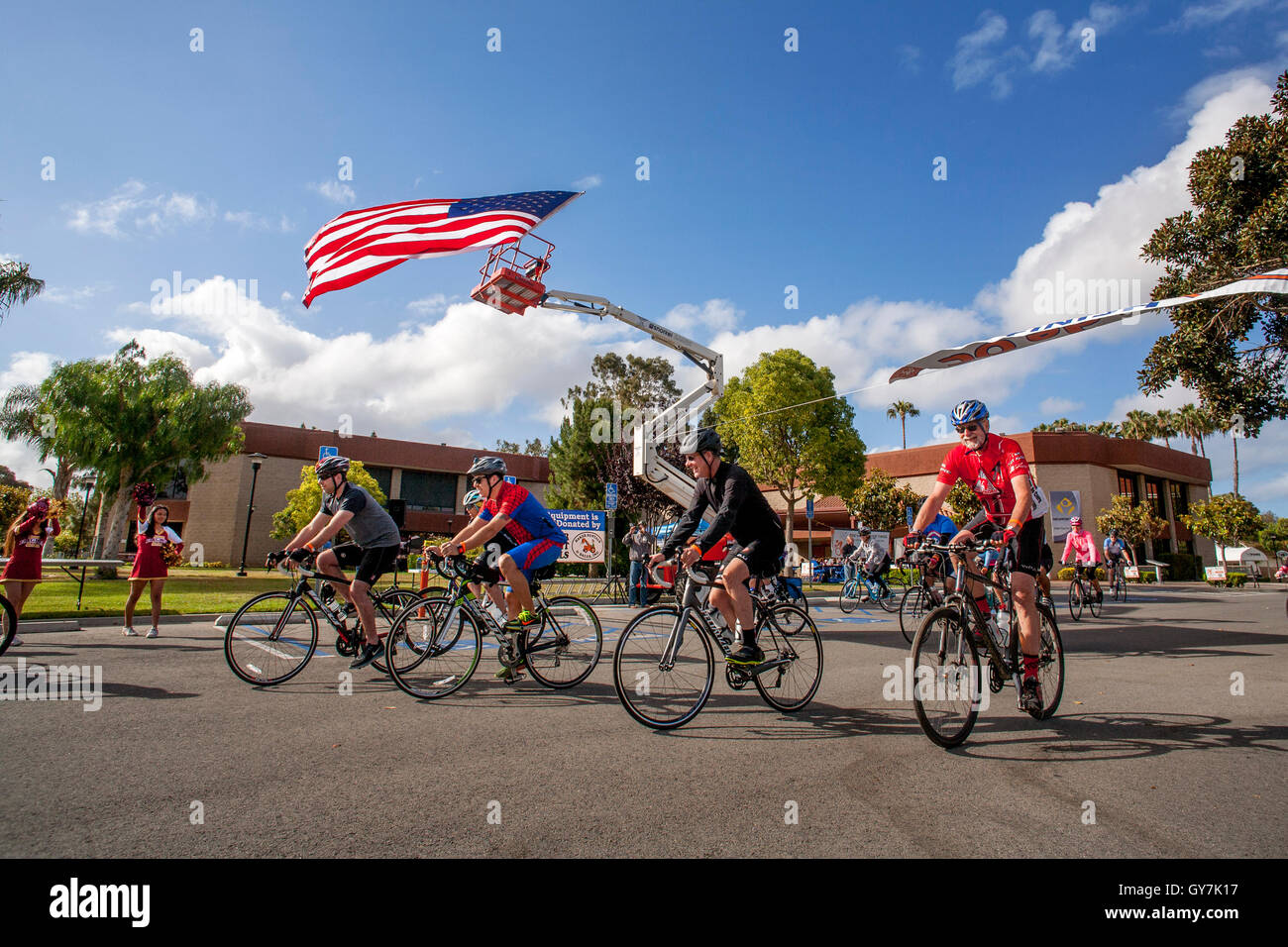 Una bandiera americana flutti nel vento come i ciclisti lascia la linea di partenza di un 55-Mile fund raising carità gara in Costa Mesa, CA. Foto Stock