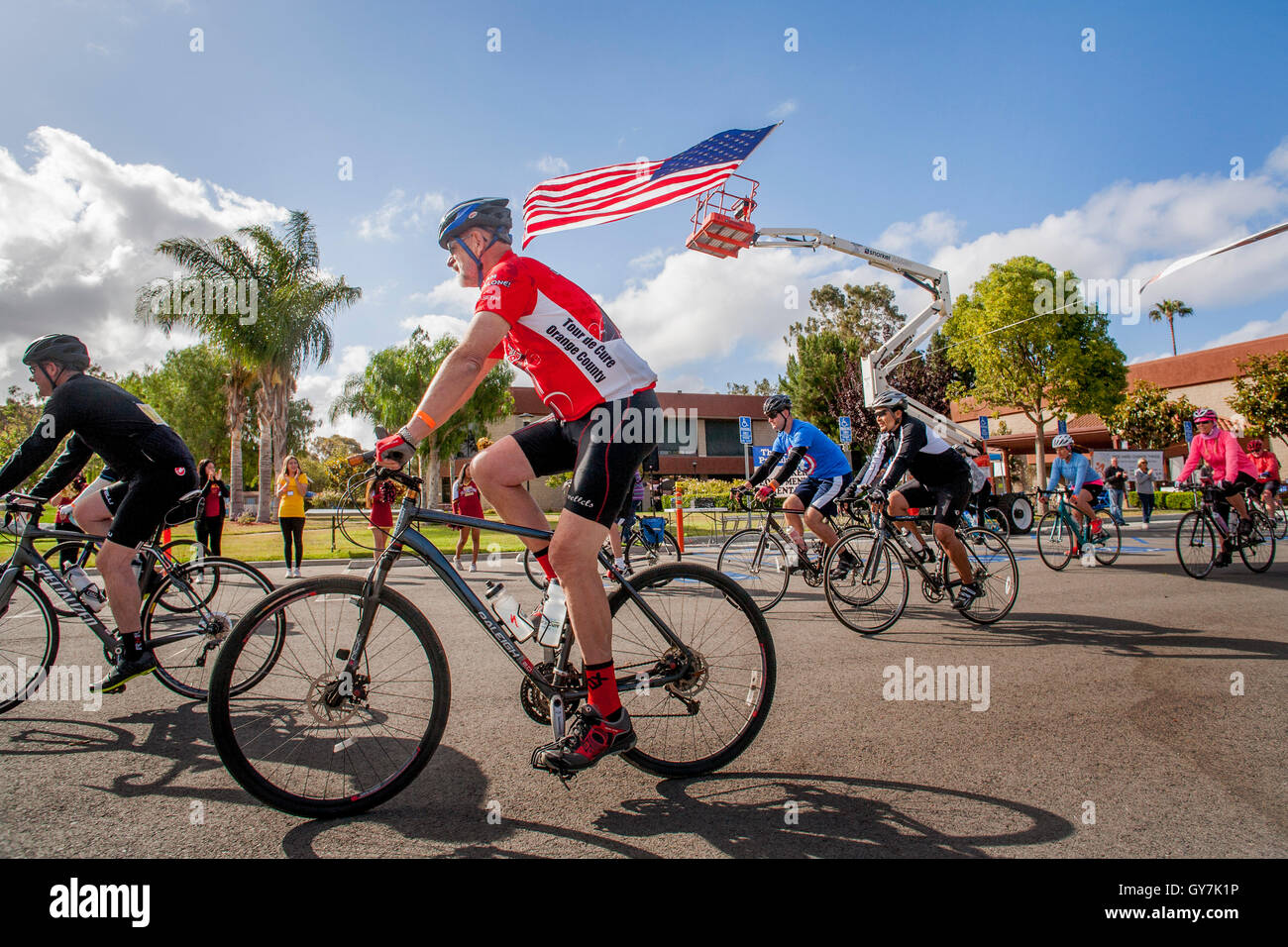 Una bandiera americana flutti nel vento come i ciclisti lascia la linea di partenza di un 55-Mile fund raising carità gara in Costa Mesa, CA. Foto Stock