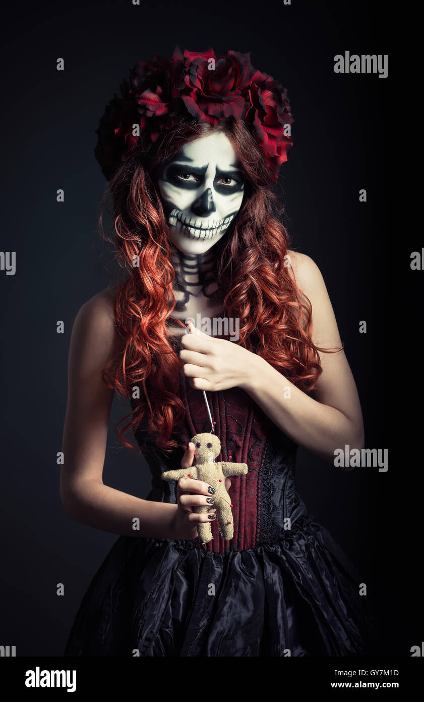 Giovane strega voodoo con trucco muertos (zucchero cranio) mantiene la bambola voodoo e ago Foto Stock