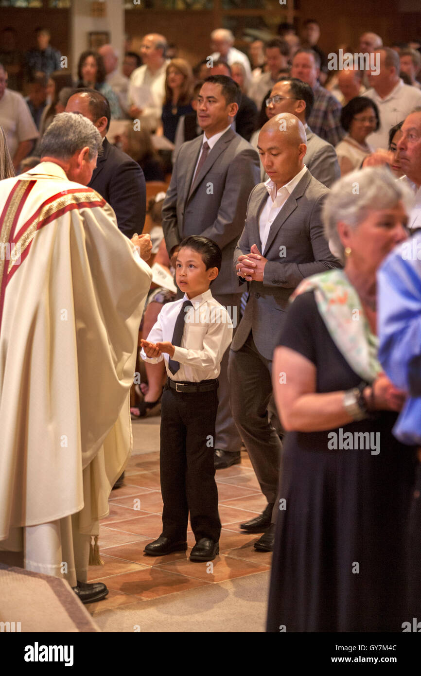 Un formalmente vestiti ispanico ragazzo riceve una benedizione all omelia  della Santa Messa di Prima Comunione in una Laguna Niguel, CA, chiesa  cattolica. La prima comunione è una cerimonia in alcune tradizioni