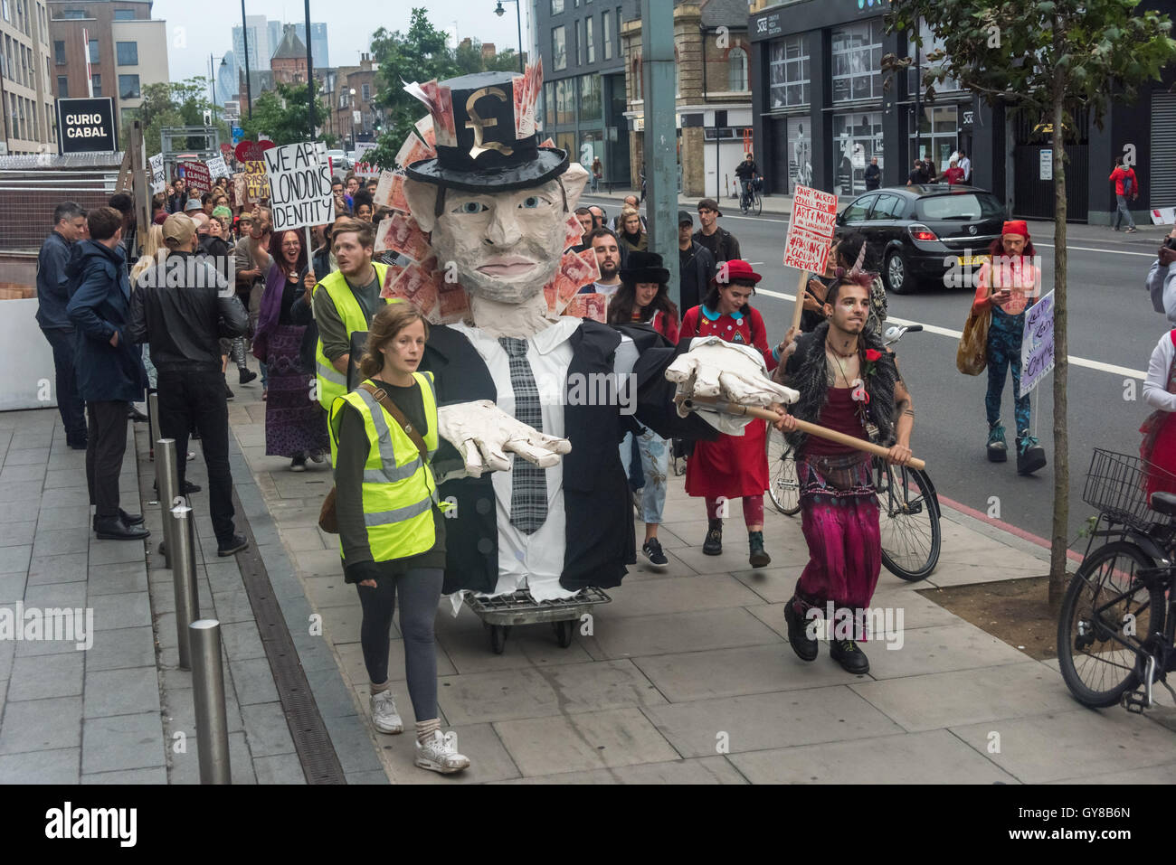 Londra, Regno Unito. 17 settembre 2016. Centinaia di soddisfare in Hoxton Square, molti indossando rosso, a marzo per sostenere il passaggio di nuvole, indipendente London music venue in Haggerston. Essi hanno marciato lungo il marciapiede al club un po' più di un miile lontano in un atmosfera di festa guidato da una grande figura di un avido capitalista con cinquanta pound note insaccata nella sua aveva e pende verso il basso la schiena e sono stati uniti in modo da parte di una band che suona su un autocarro. Passare nubi ospitato più di 10.000 eventi culturali e musicali sin dalla sua apertura nel 2006 si celebra il suo decimo anniversario quando ha appreso che il suo proprietario aveva segretamente Foto Stock